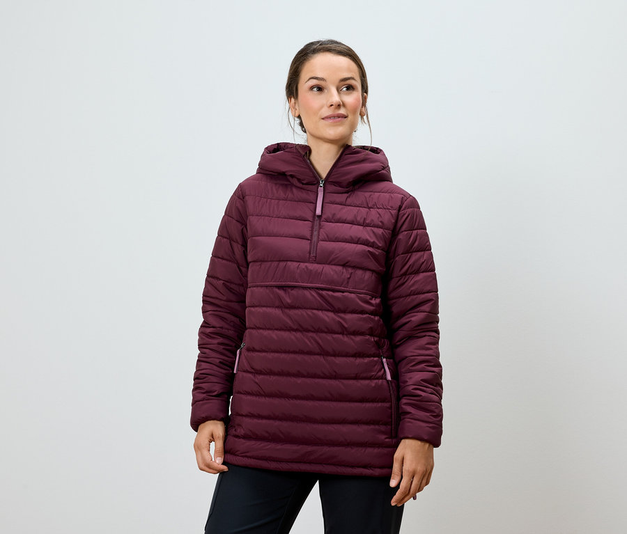 Žena pózuje v bordovej prešívanej bunde s kapucňou a čiernych nohaviciach.