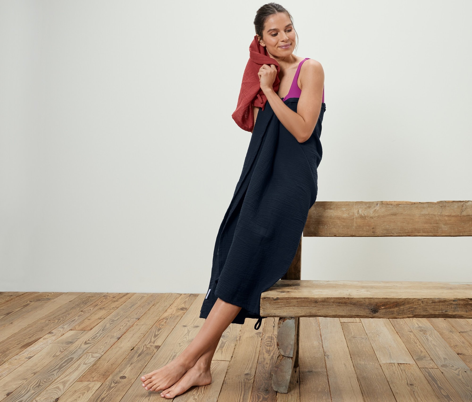 Žena si suší vlasy s mušelínovými uterákmi, 2 ks, sediac na drevenej lavici.