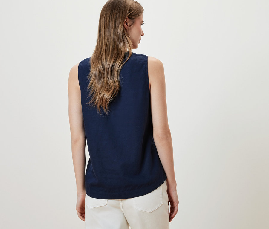 Žena má na sebe bezrukávovú ľanovú blúzku, námornícka modrá a biele nohavice.