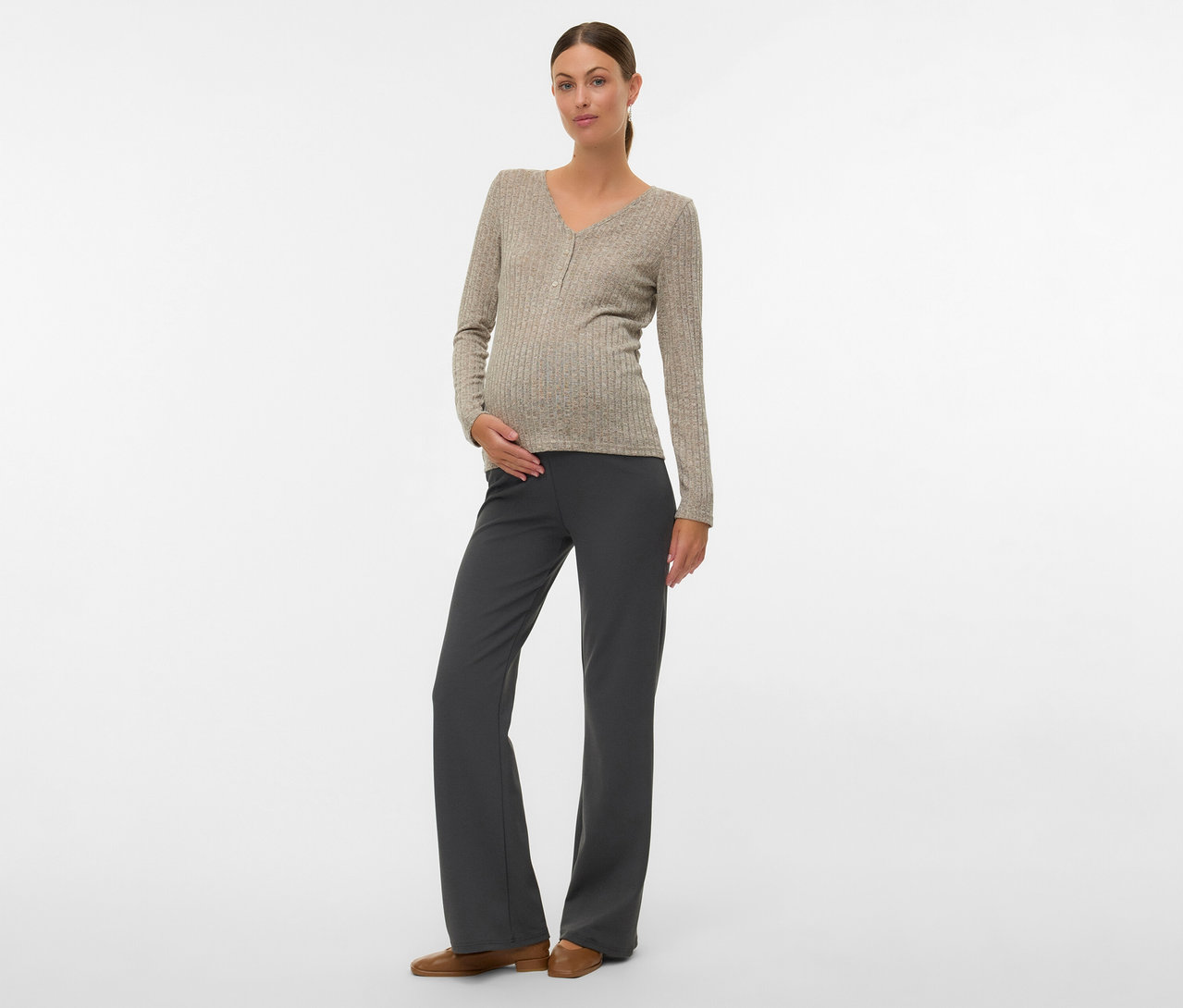 Žena s drdolom má na sebe tričko MAMALICIOUS »MLPAMMIE LIA«, sivé nohavice a hnedé topánky, ruku na bruchu.