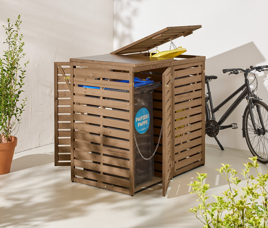 Hnedý drevený box na odpadkové koše s otvorenými dverami a vekom stojí vedľa čierneho bicykla.