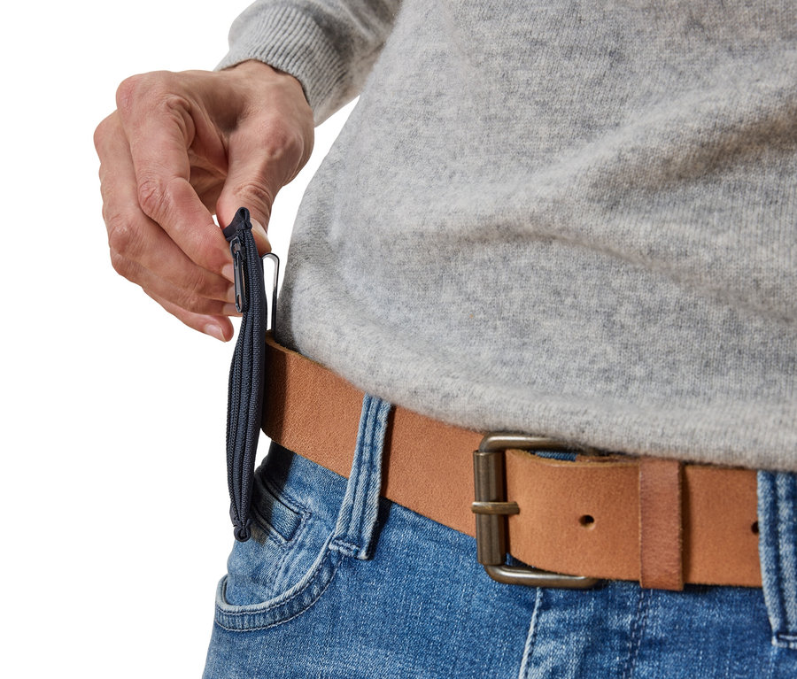 Detailný záber osoby pripínajúcej úzke, tmavomodré vrecko na zips na hnedý kožený opasok, ktorý sa nosí na modrých džínsoch.