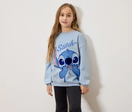 Dievča s dlhými blond vlasmi má na sebe svetlomodrú mikinu s potlačou Stitch a čierne legíny.