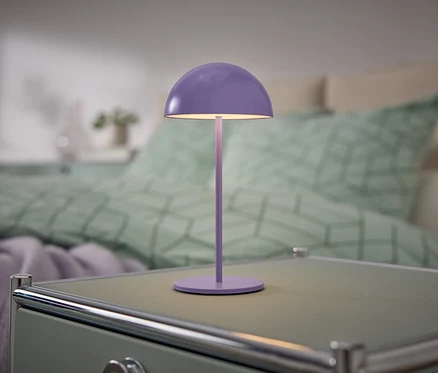 Fialová lampa stojí na nočnom stolíku vedľa postele.