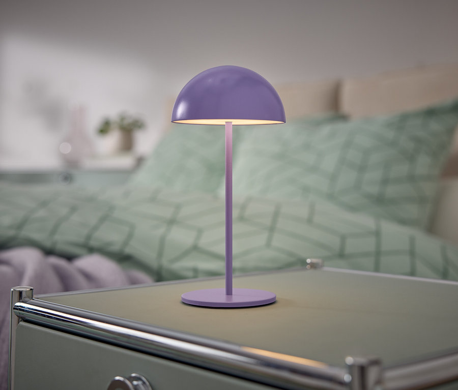 Fialová lampa stojí na nočnom stolíku vedľa postele.