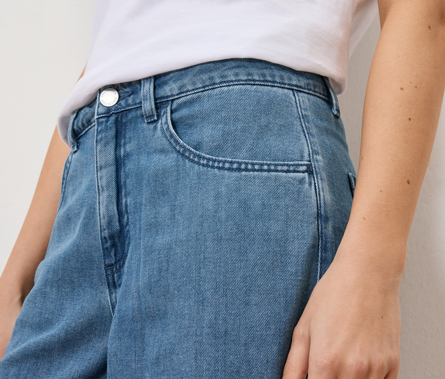 Detailný záber ženy v svetlomodrých džínsoch a bielom tričku.