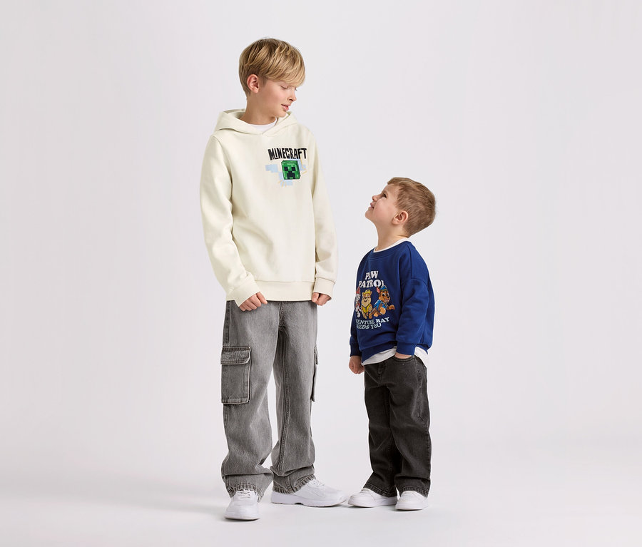 Dvaja chlapci stoja na bielom pozadí. Väčší chlapec má na sebe detskú mikinu s kapucňou MINECRAFT so zdrsnenou vnútornou stranou.