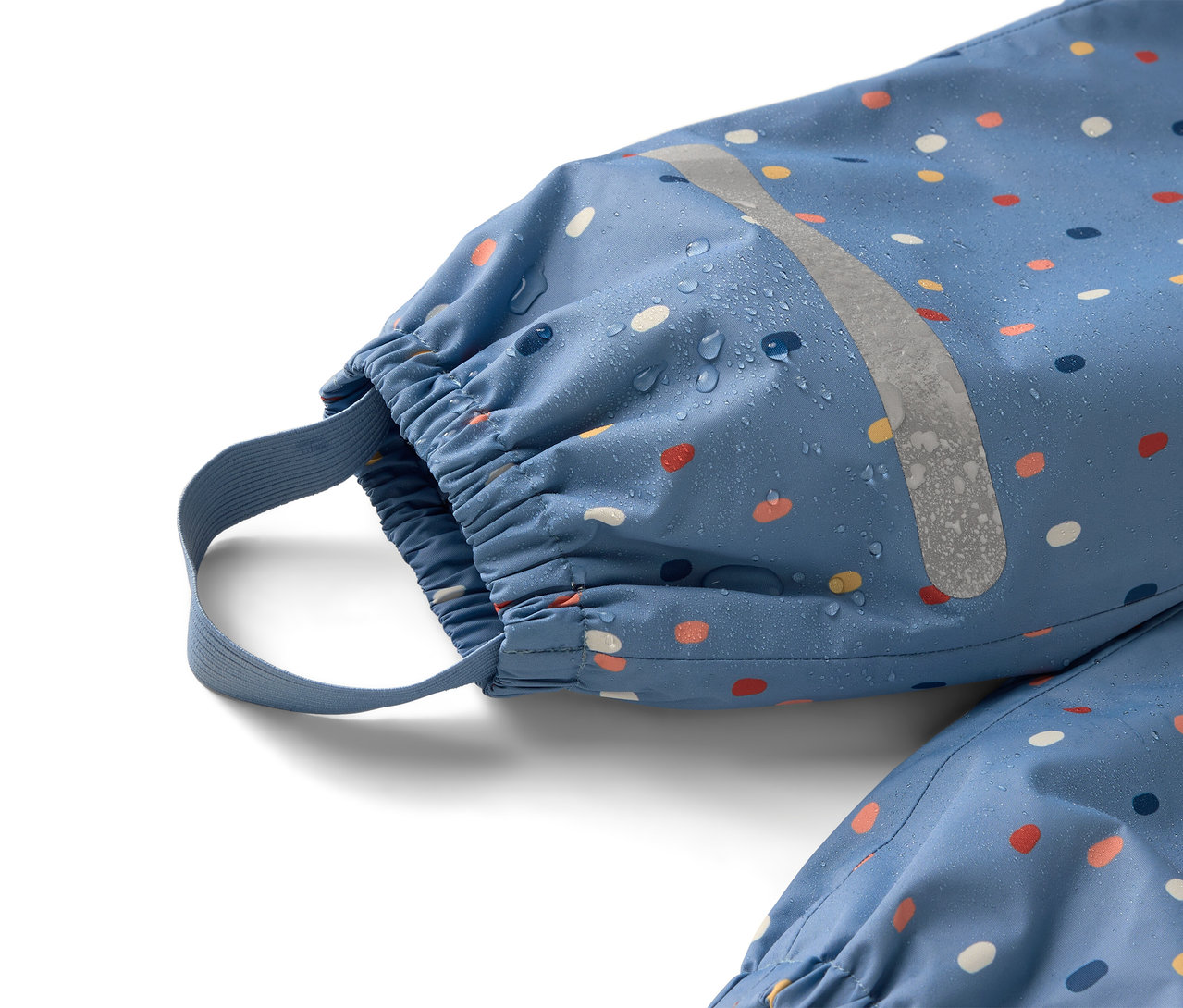 Detailný záber na modrý overal do dažďa s farebnými bodkami a reflexným prúžkom, na ktorom sú viditeľné kvapky vody.