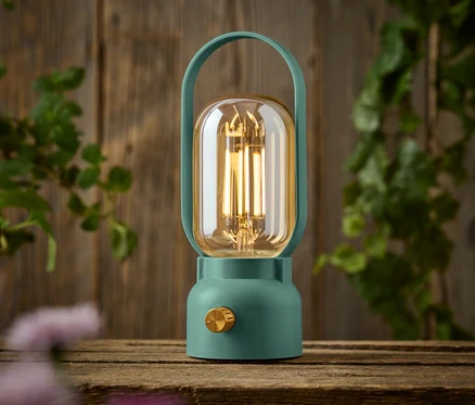 Zelená lampa so zlatým gombíkom stojí na drevenom stole.