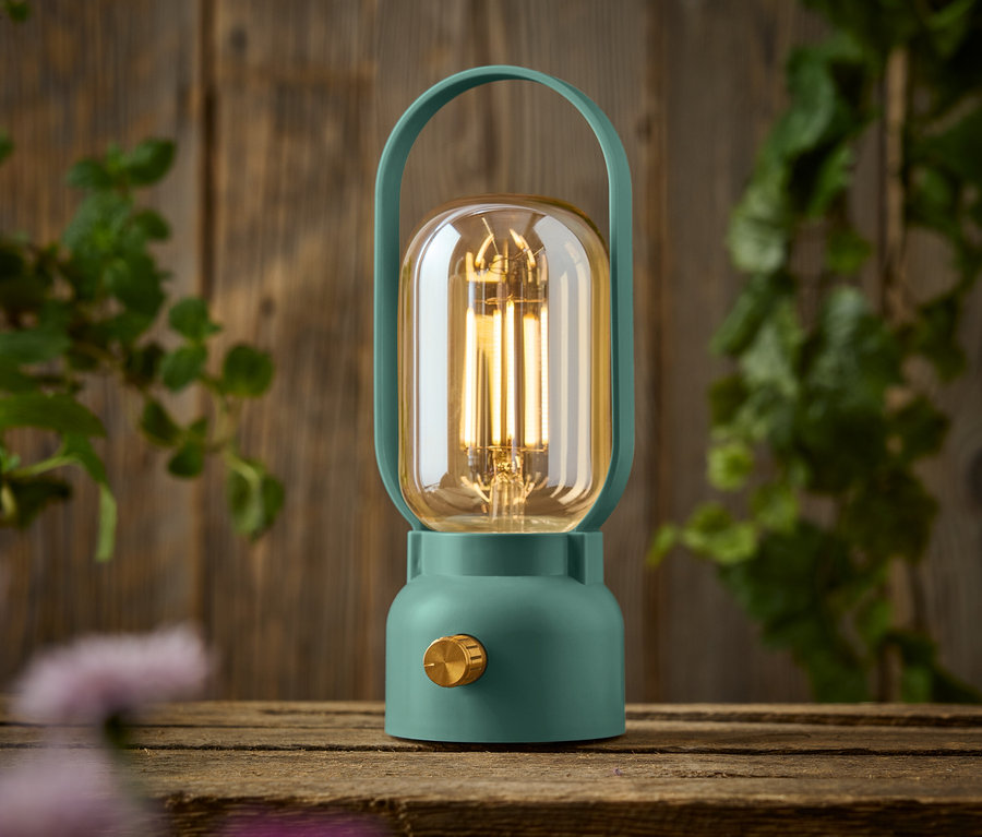 Zelená lampa so zlatým gombíkom stojí na drevenom stole.