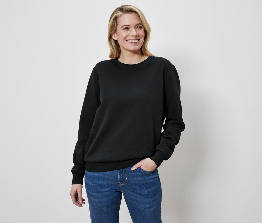 Žena s blond vlasmi má na sebe čierny sveter a džínsy.