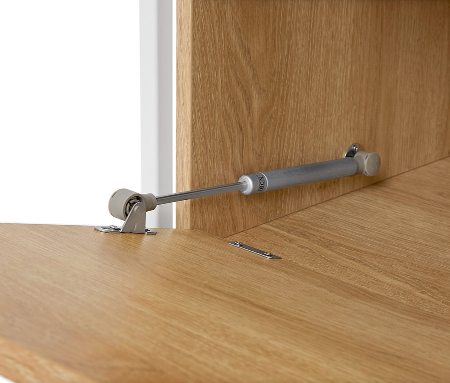 Detailný pohľad na nábytkový pánt na svetlohnedom drevenom povrchu.