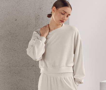 Žena pózuje v béžovej obzvlášť mäkkej teplákovej súprave, ktorá sa skladá z mikiny a nohavíc.