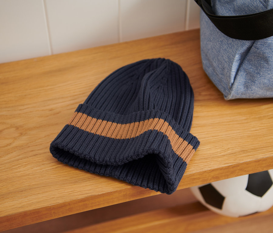 Na drevenej polici leží pletená čiapka a vedľa nej športová taška.