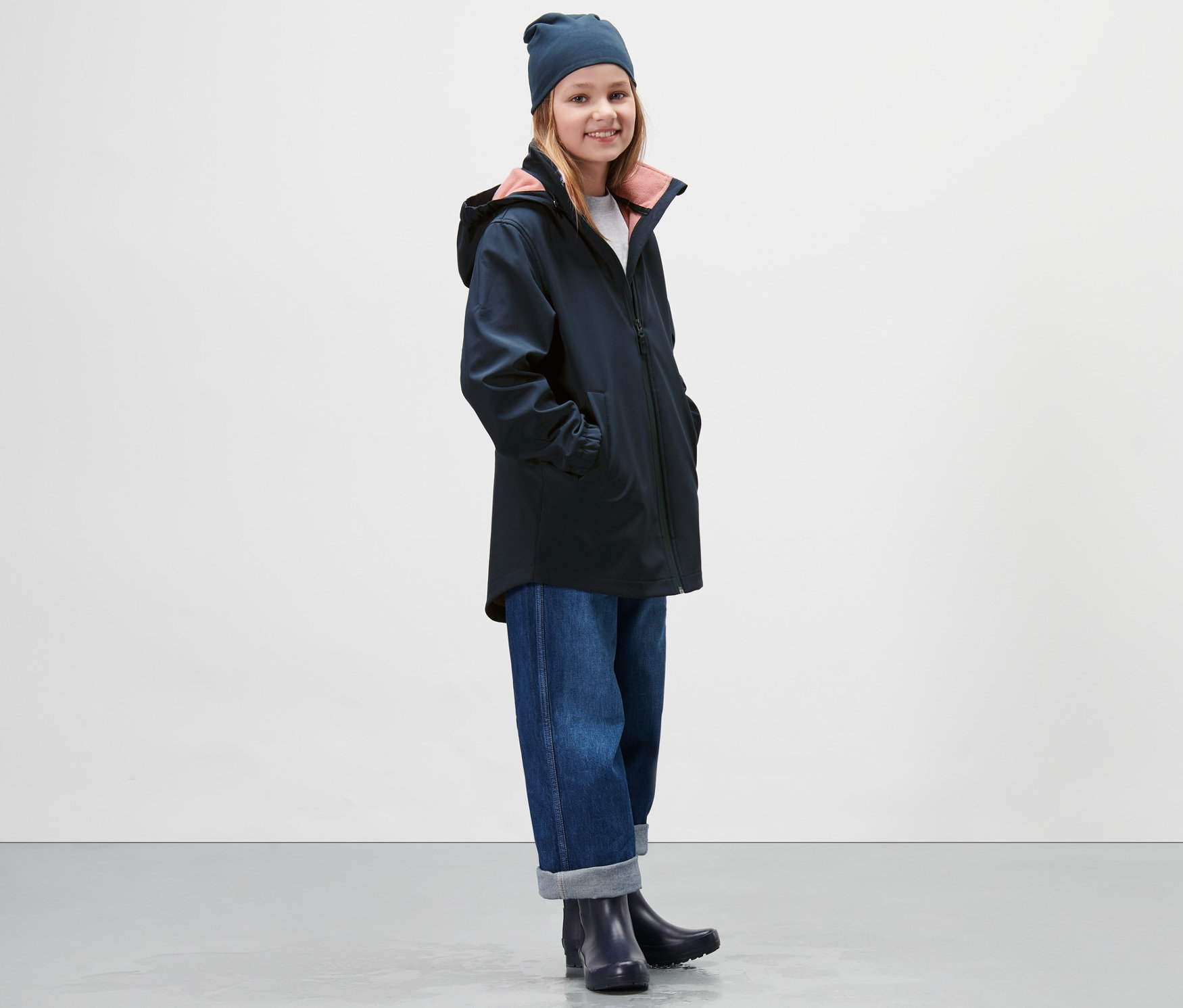 Dievča má na sebe tmavomodrý softshellový kabát, džínsy a čiapku.