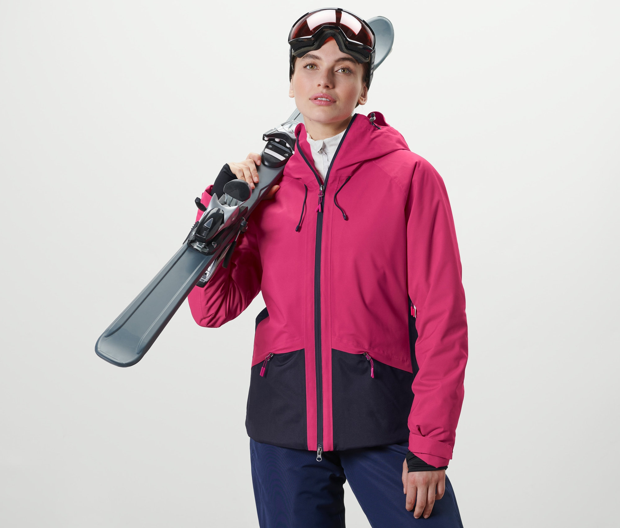 Žena drží lyže cez rameno. Má na sebe lyžiarsku bundu.