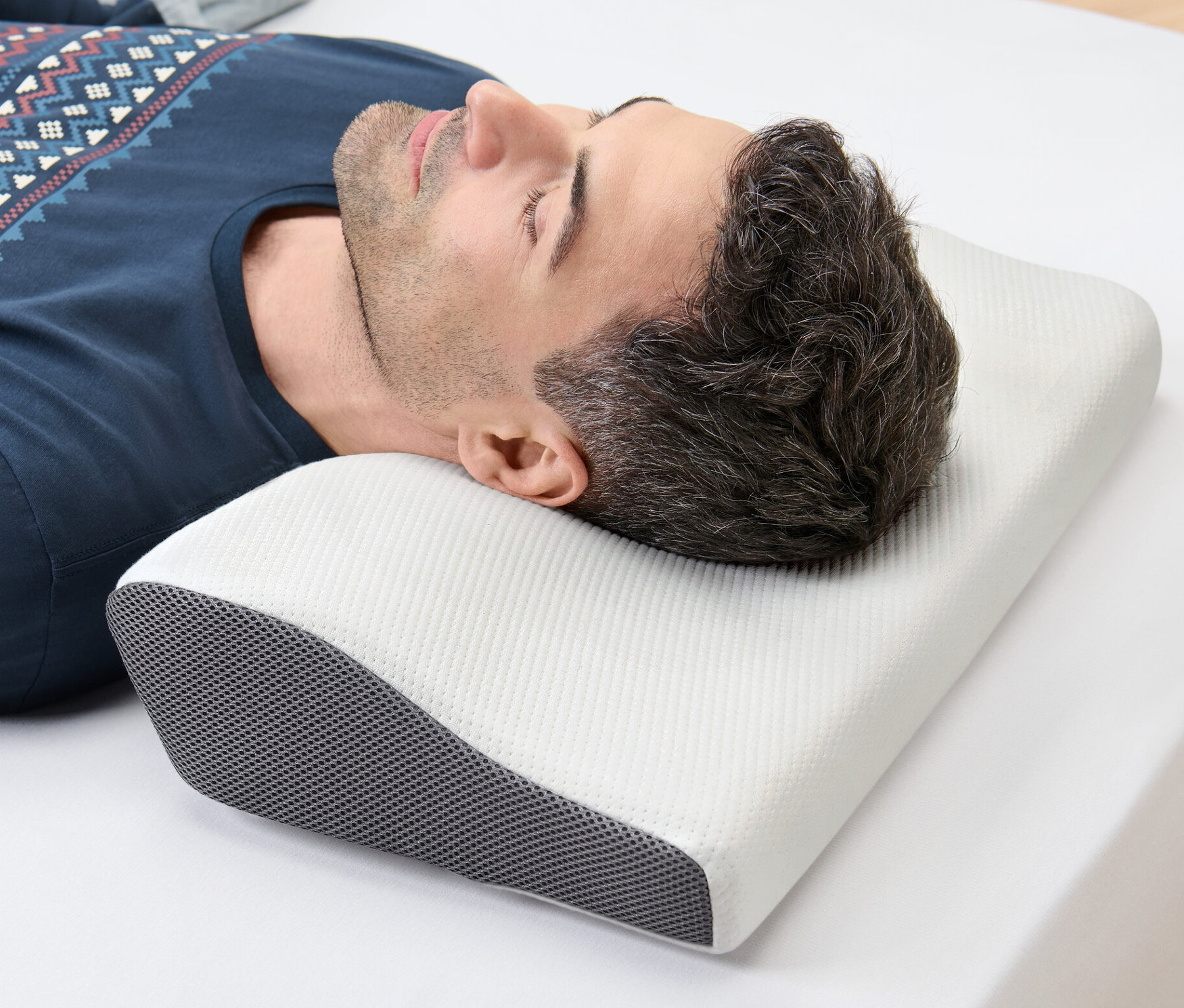 Muž leží na boku na bielej plachte a hlavu má na vankúši na oporu krčnej chrbtice.