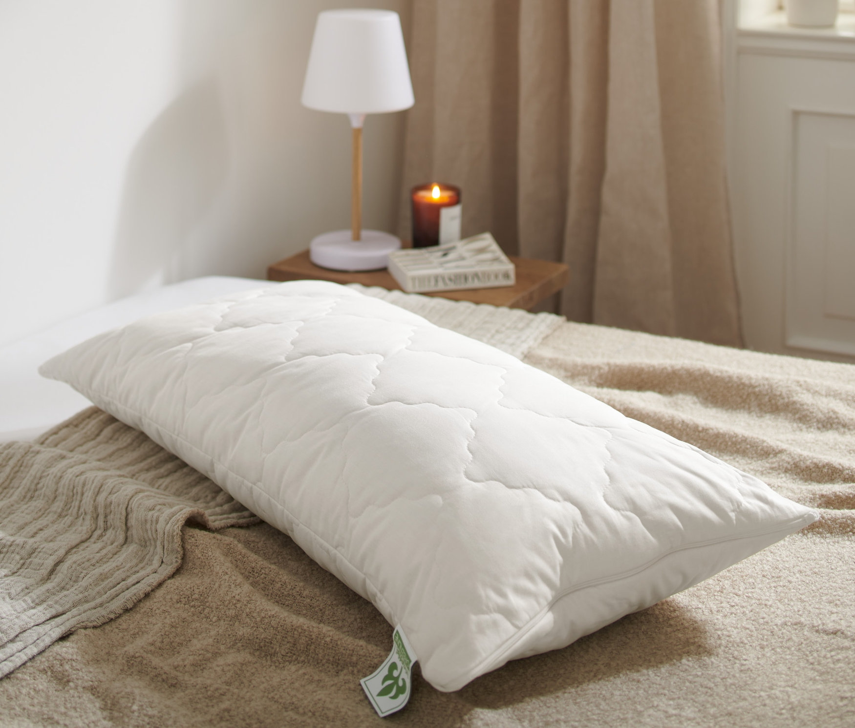 Na posteli leží biely prešívaný vankúš s levanduľou irisette® greenline cca 80 x 40 cm.