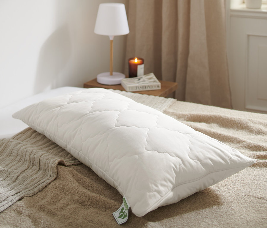 Na posteli leží biely prešívaný vankúš s levanduľou irisette® greenline cca 80 x 40 cm.