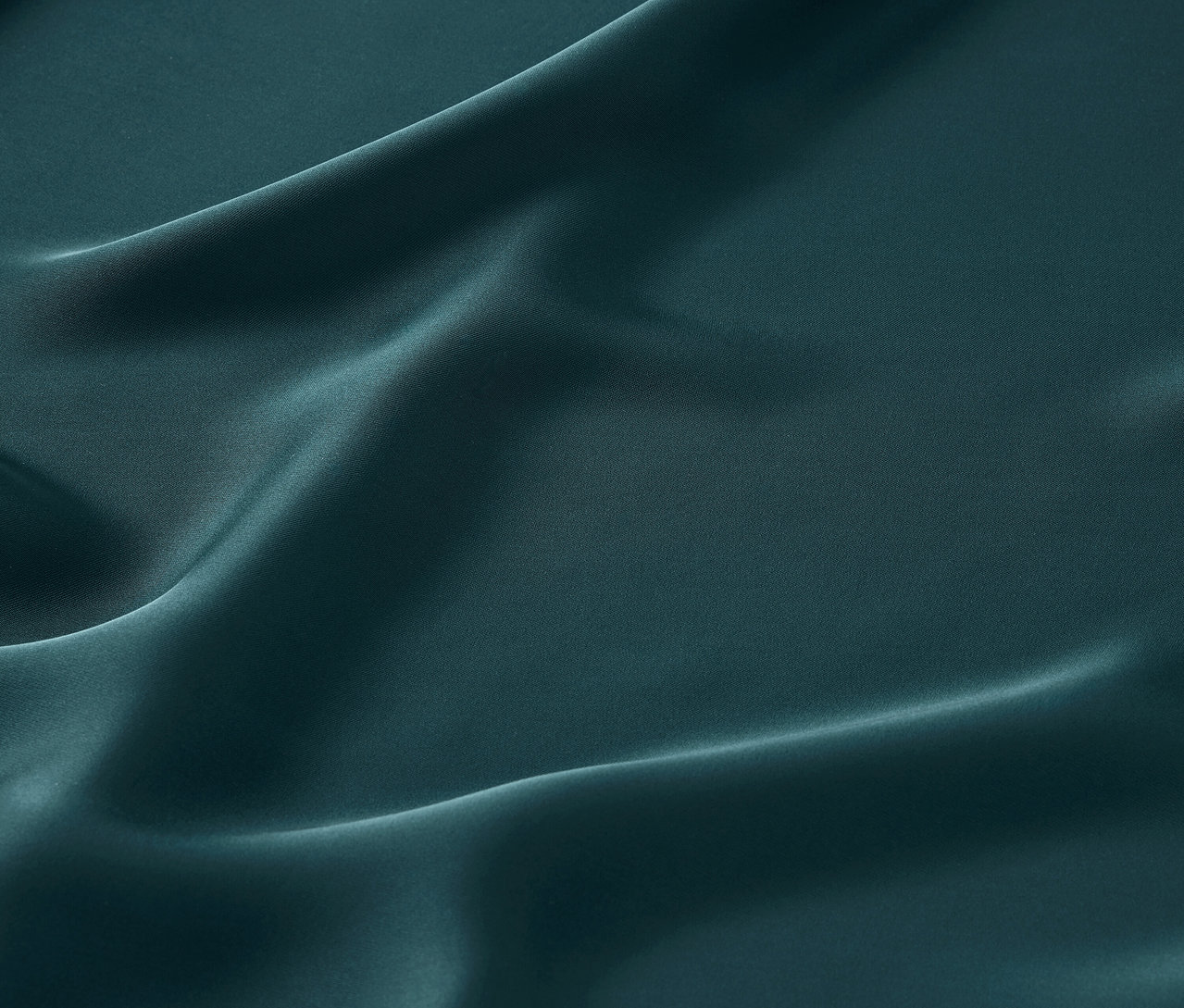 Detailný záber na smaragdovo zelenú saténovú látku s jemnými záhybmi.