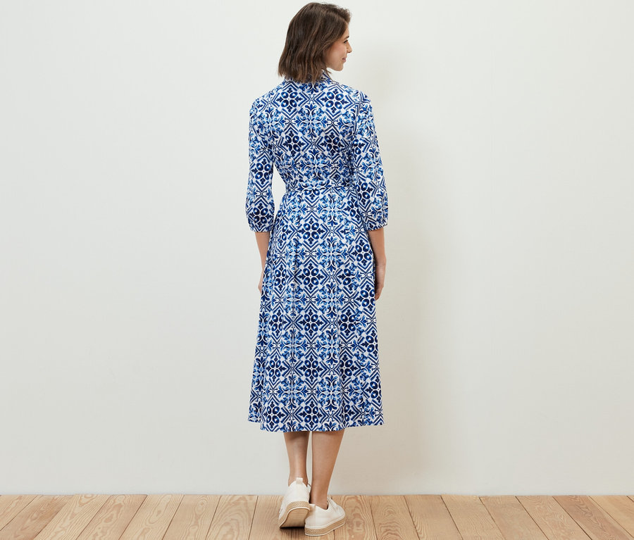 Žena stojí chrbtom k fotoaparátu a má na sebe midi šaty s potlačou.