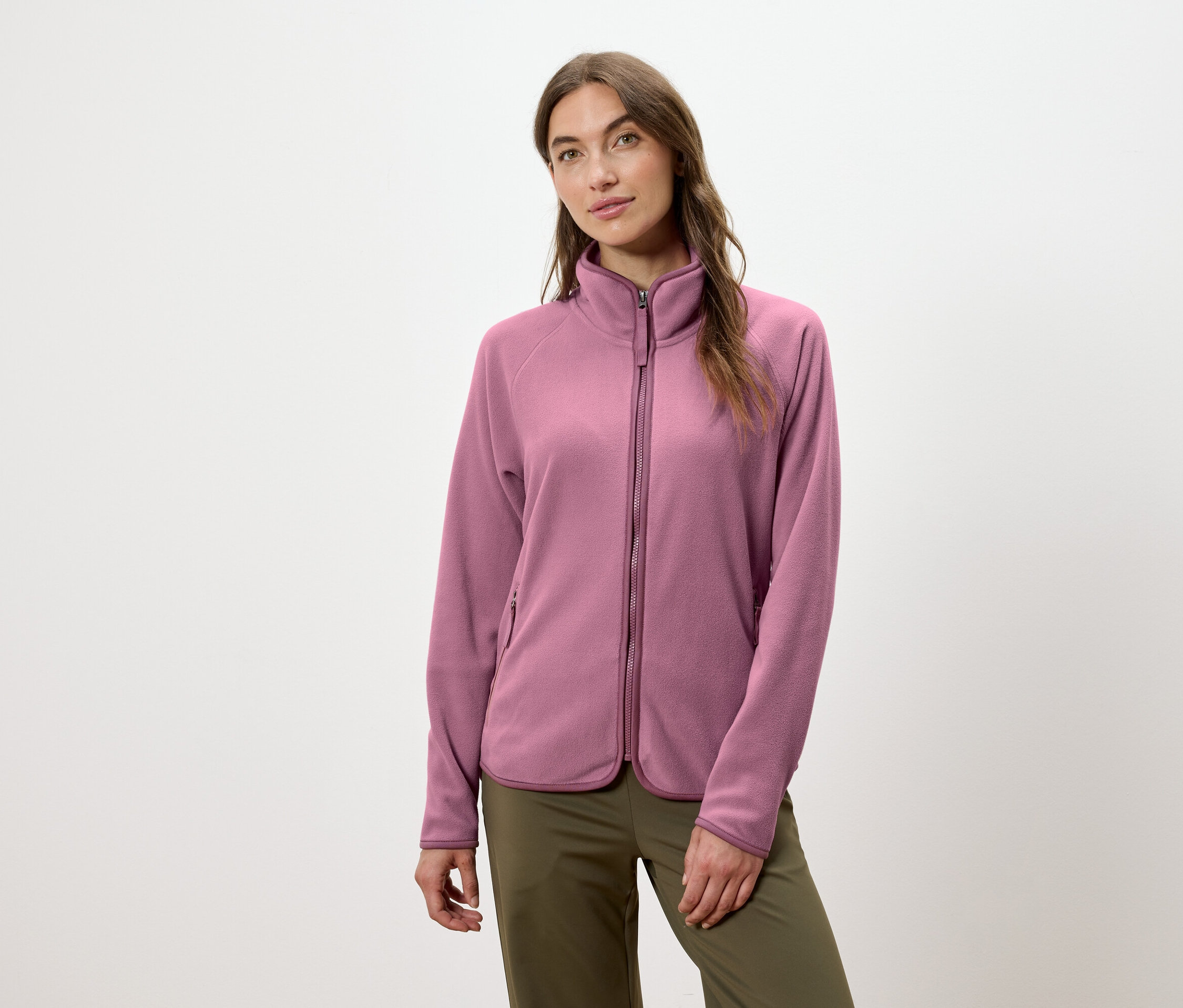 Žena má na sebe ružovú fleecovú bundu na zips a zelené nohavice.