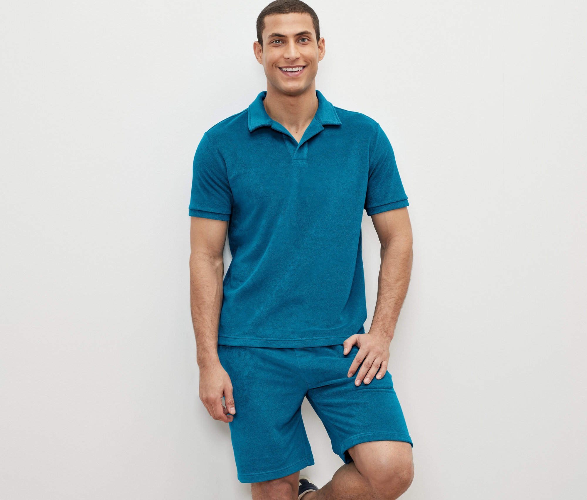 Muž pózuje v petrolejovej froté polokošeli a šortkách.