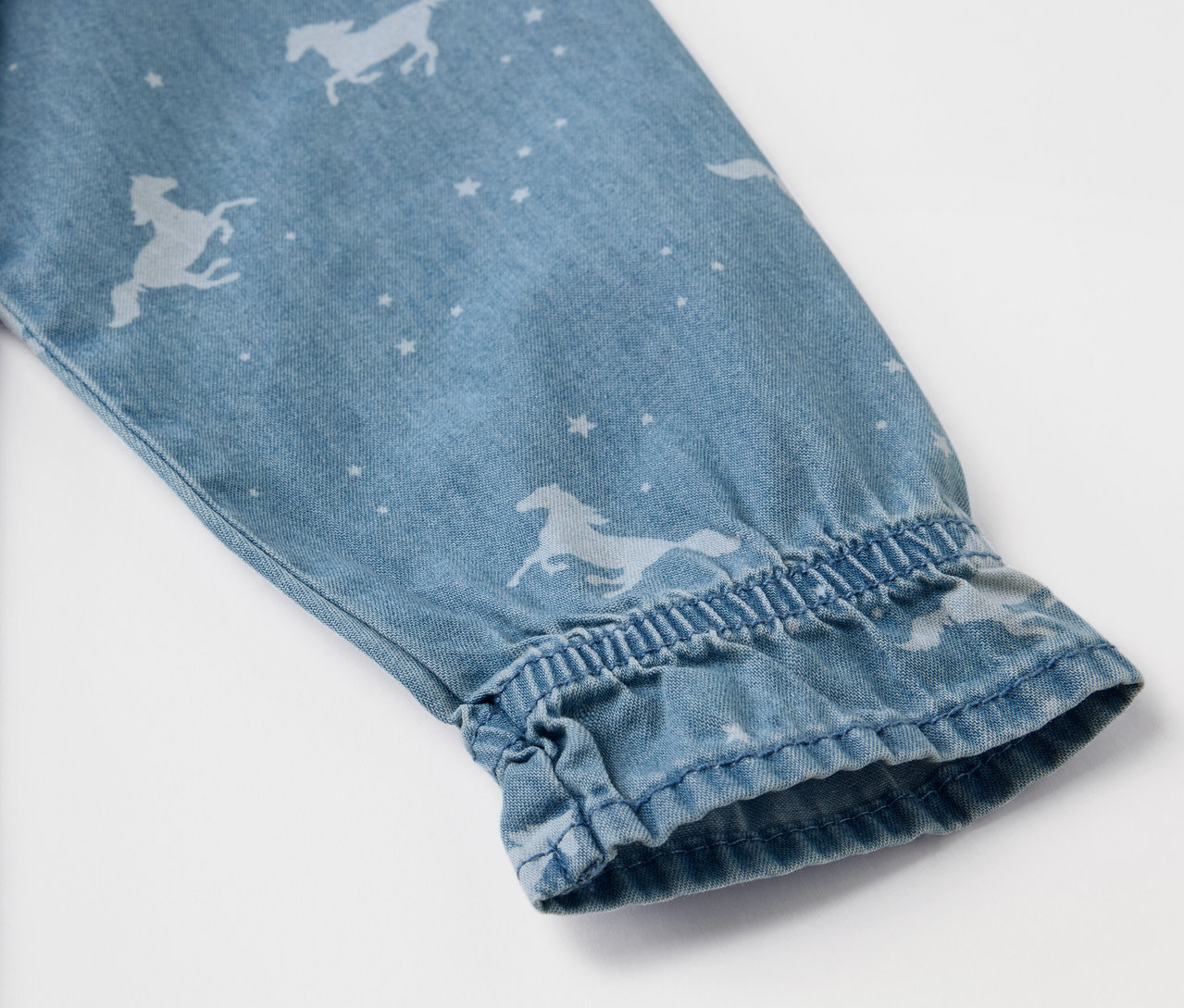 Detail rukáva džínsových šiat s potlačou koní a hviezd.