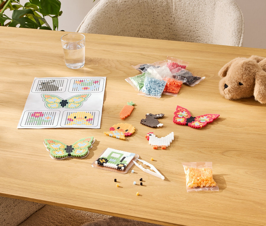 Stôl so súpravou na výrobu žehličkových korálikov, vrátane šablón, hotových vzorov a sortimentu farieb vo vreckách.