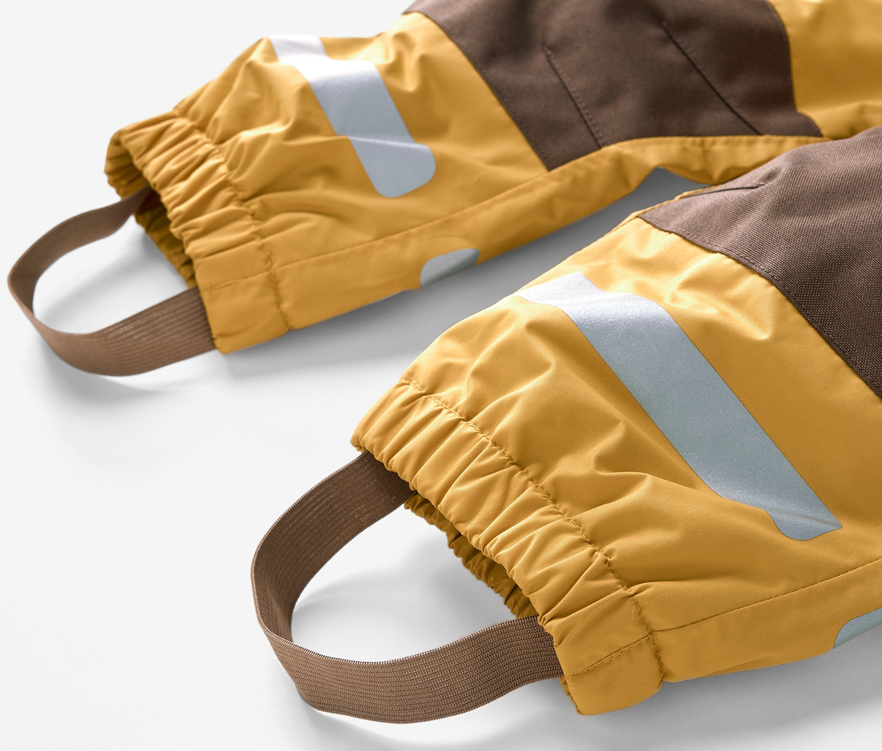 Detail detskej kombinézy do dažďa s hnedými a žltými blokmi a elastickými pásikmi na nohy.