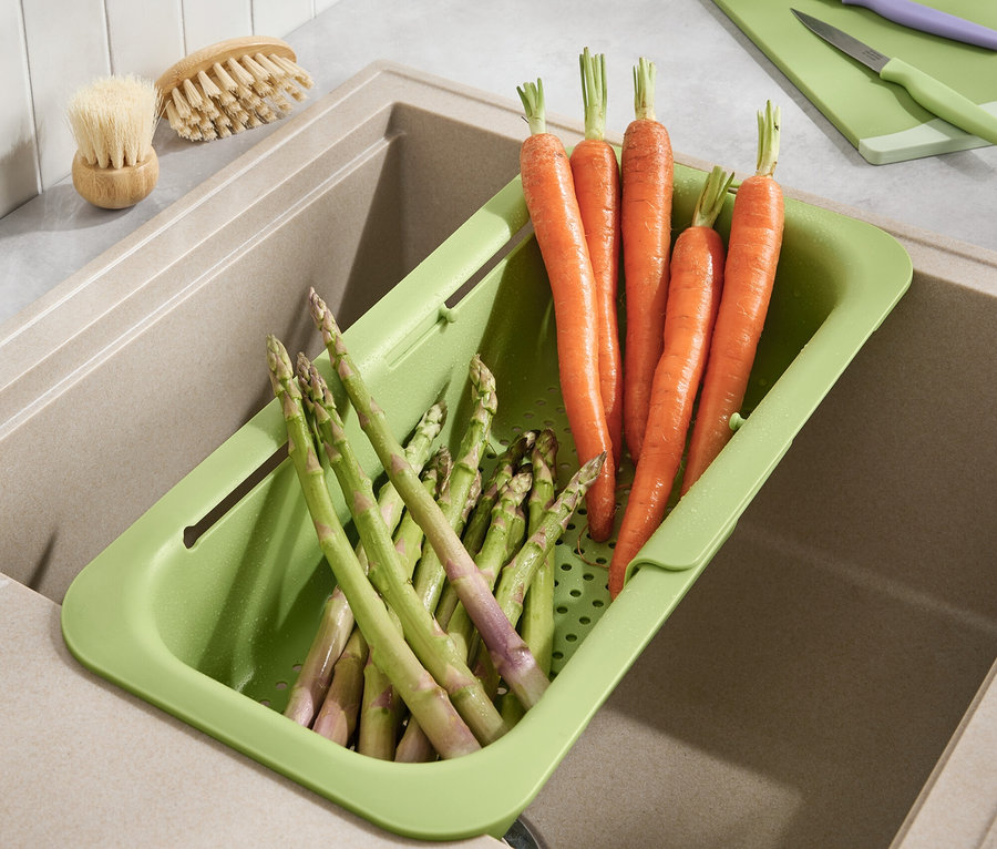 Mrkva a špargľa ležia v zelenom odkvapkávači v umývadle.