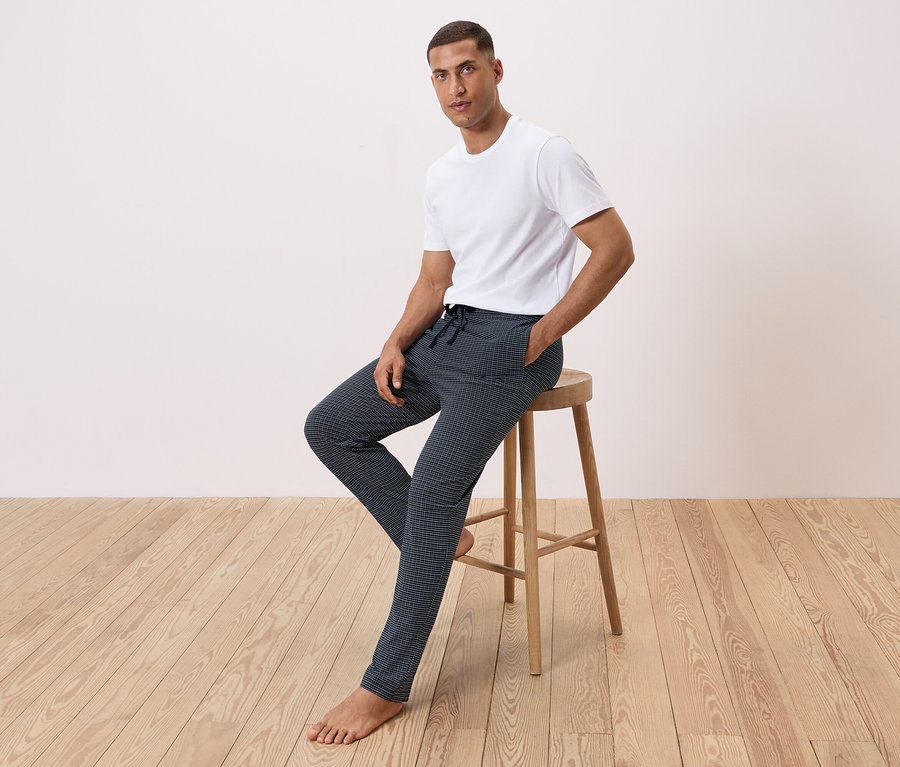 Muž sedí na stoličke, má na sebe biele tričko a vzorované nohavice.