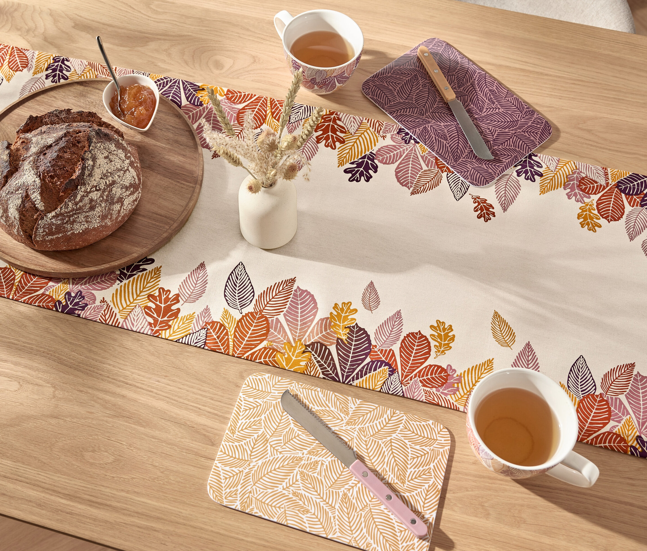 Chlieb na drevenej doske a šálka čaju na obruse so vzorom listov.