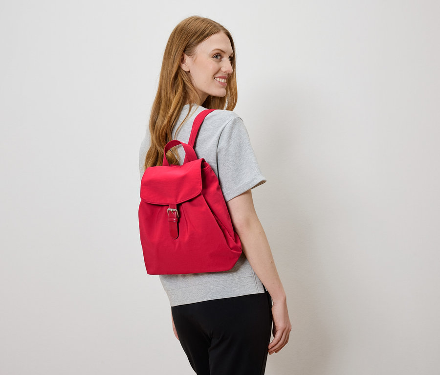 Žena s červeným batohom na chrbte sa pozerá doľava.