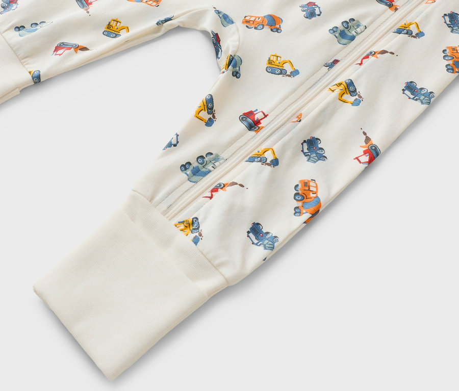 Detailný záber na overal s dlhým rukávom, zapínaním na zips a vzorom stavebných vozidiel.