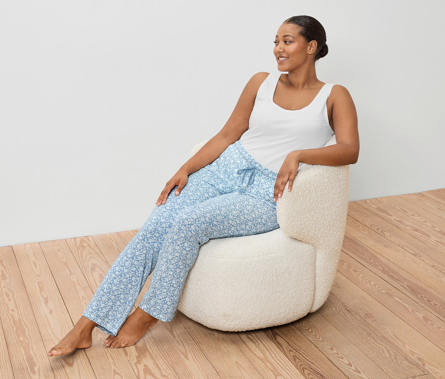 Žena sedí v kresle a má na sebe biele tielko a modré nohavice.