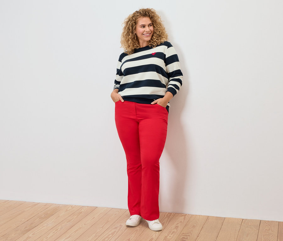 Žena s kučeravými vlasmi má na sebe pruhovaný top a červené nohavice.