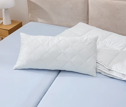 Biely vankúš Cell Solution® s rozmermi 80 x 40 cm leží na modrej posteli vedľa bielej periny.