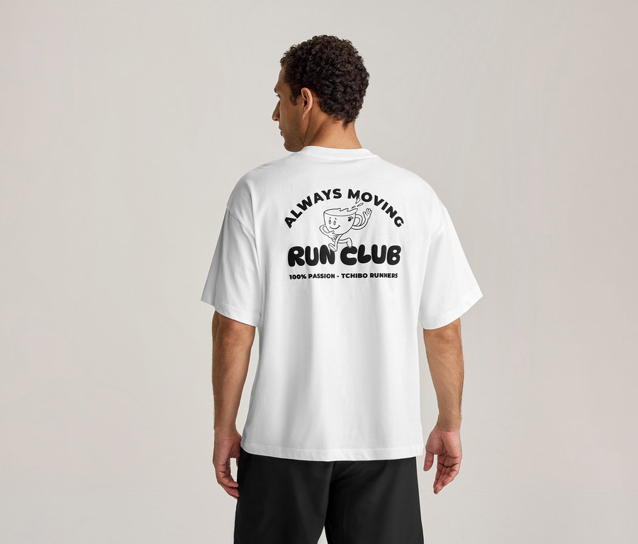 Muž zozadu v bielom športovom tričku s čiernou potlačou "ALWAYS MOVING RUN CLUB" a bežiacou šálkou kávy.