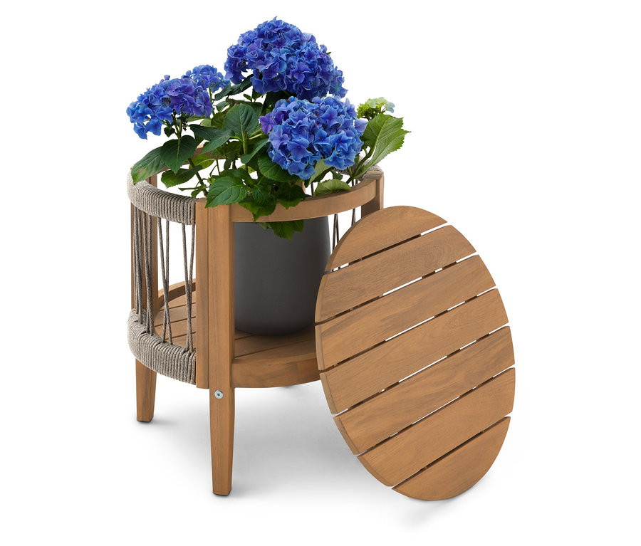 Modrý hortenziový ker v sivom kvetináči na dvojposchodovom drevenom stolíku s oválnou doskou stola stojacou vedľa.