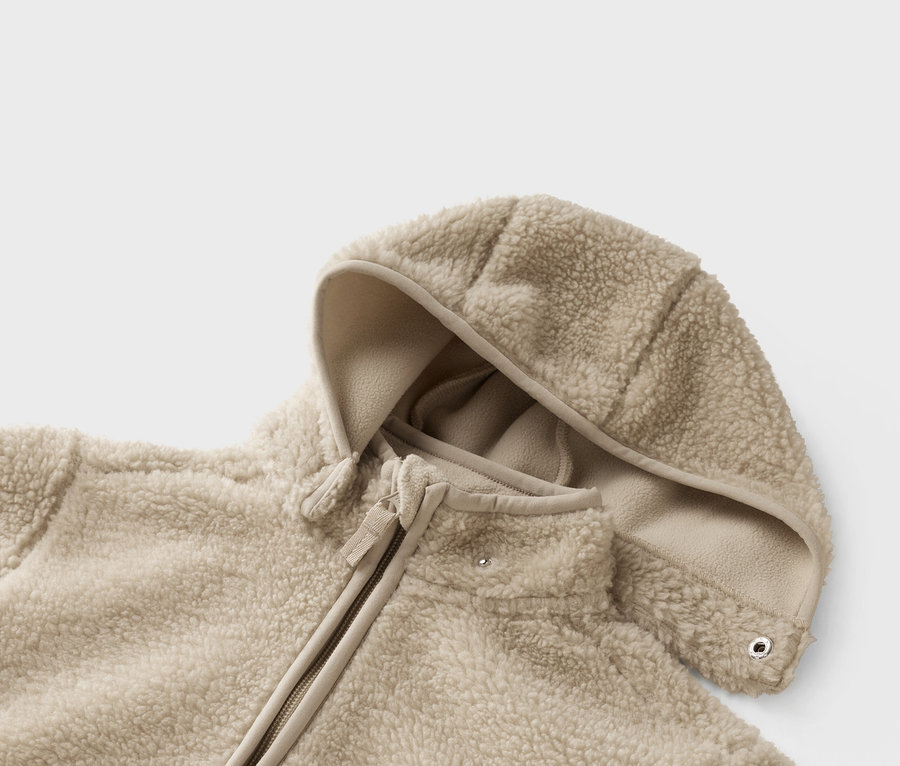 Detail béžovej teddy fleecovej bundy s kapucňou a zipsom.