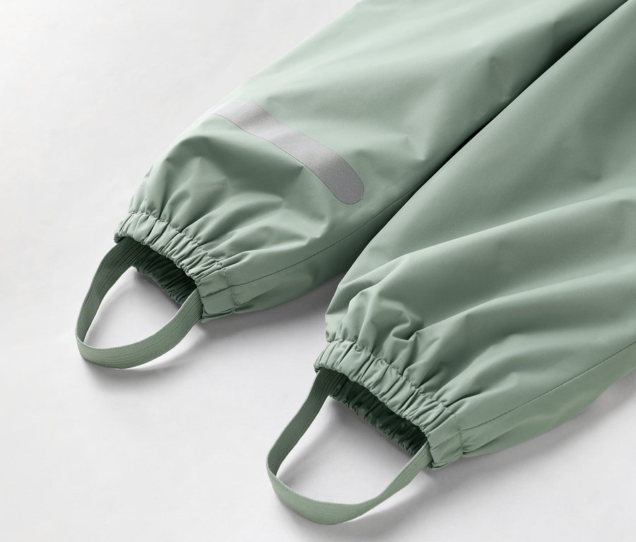 Detailný záber spodnej časti svetlozelených nohavíc s elastickými manžetami a slučkami na nohy.