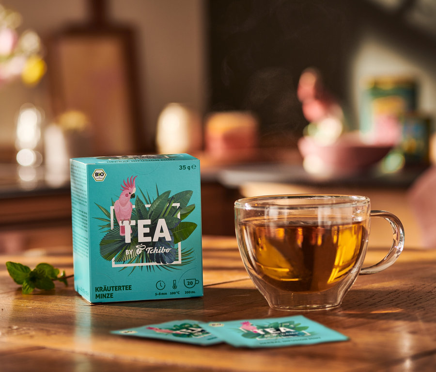 Balenie BIO TEA by Tchibo mäta vedľa šálky čaju a lístkov mäty na drevenom stole.