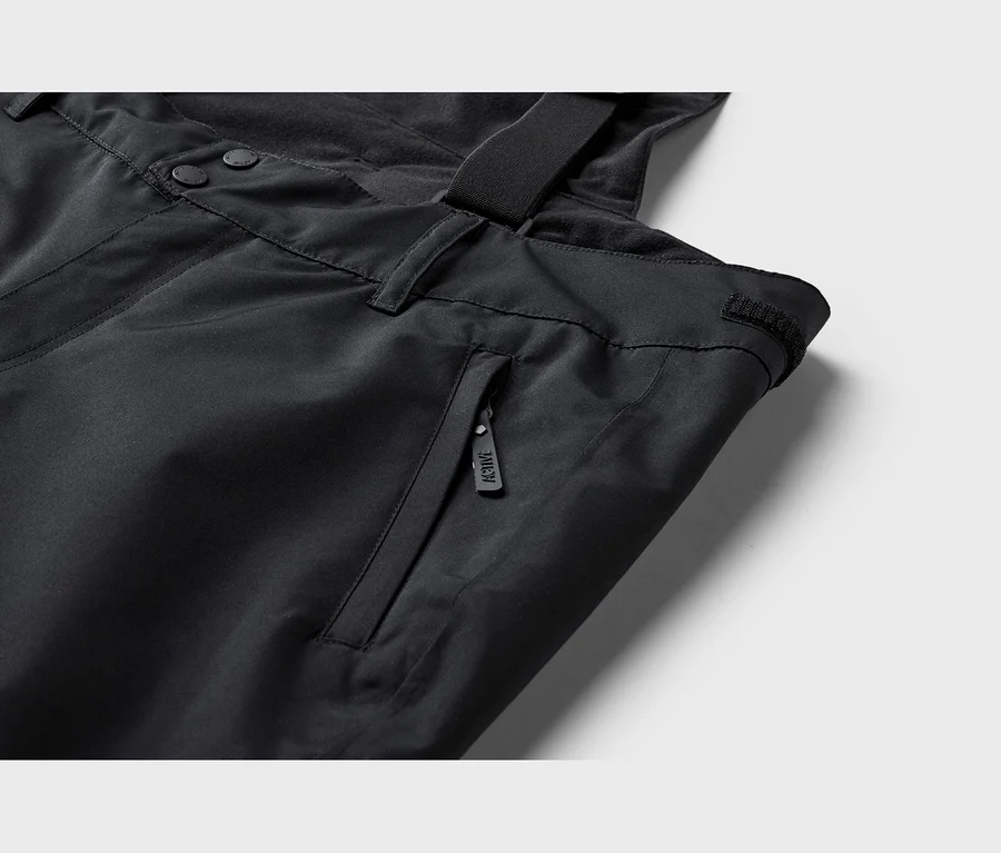 Detail čiernych technických nohavíc s gombíkmi, vreckom na zips s nápisom „ACTIVE“ a trakom.