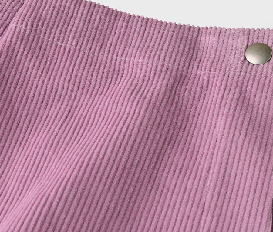 Detail ružovej menčestrovej látky s vertikálnymi rebrami a strieborným gombíkom vpravo hore, ktorý zaisťuje prekrývajúci sa okraj.