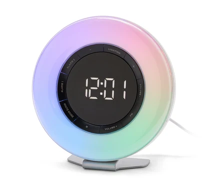 Okrúhly budík s digitálnym displejom zobrazujúcim 12:01 a dúhovým podsvietením po obvode, stojaci na striebornom podstavci.
