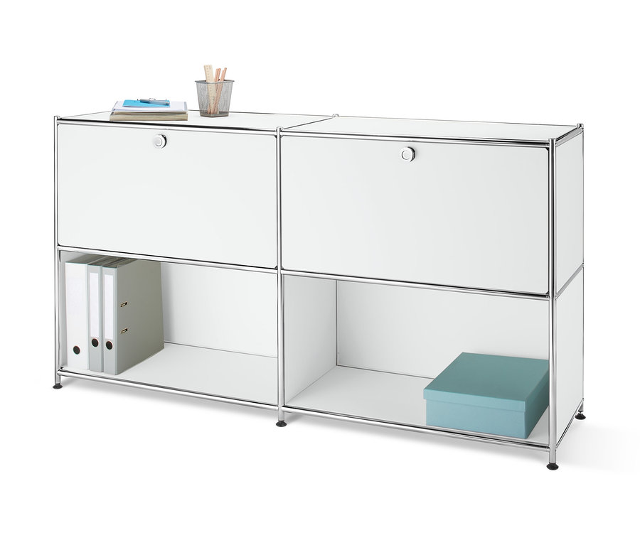 Čelný pohľad na kovovú odkladaciu skrinku s 2 nastaviteľnými výklopnými priehradkami, na ktorej leží zápisník a pohár s ceruzkami. V otvorenej polici sú dva zakladače a modrá škatuľa.