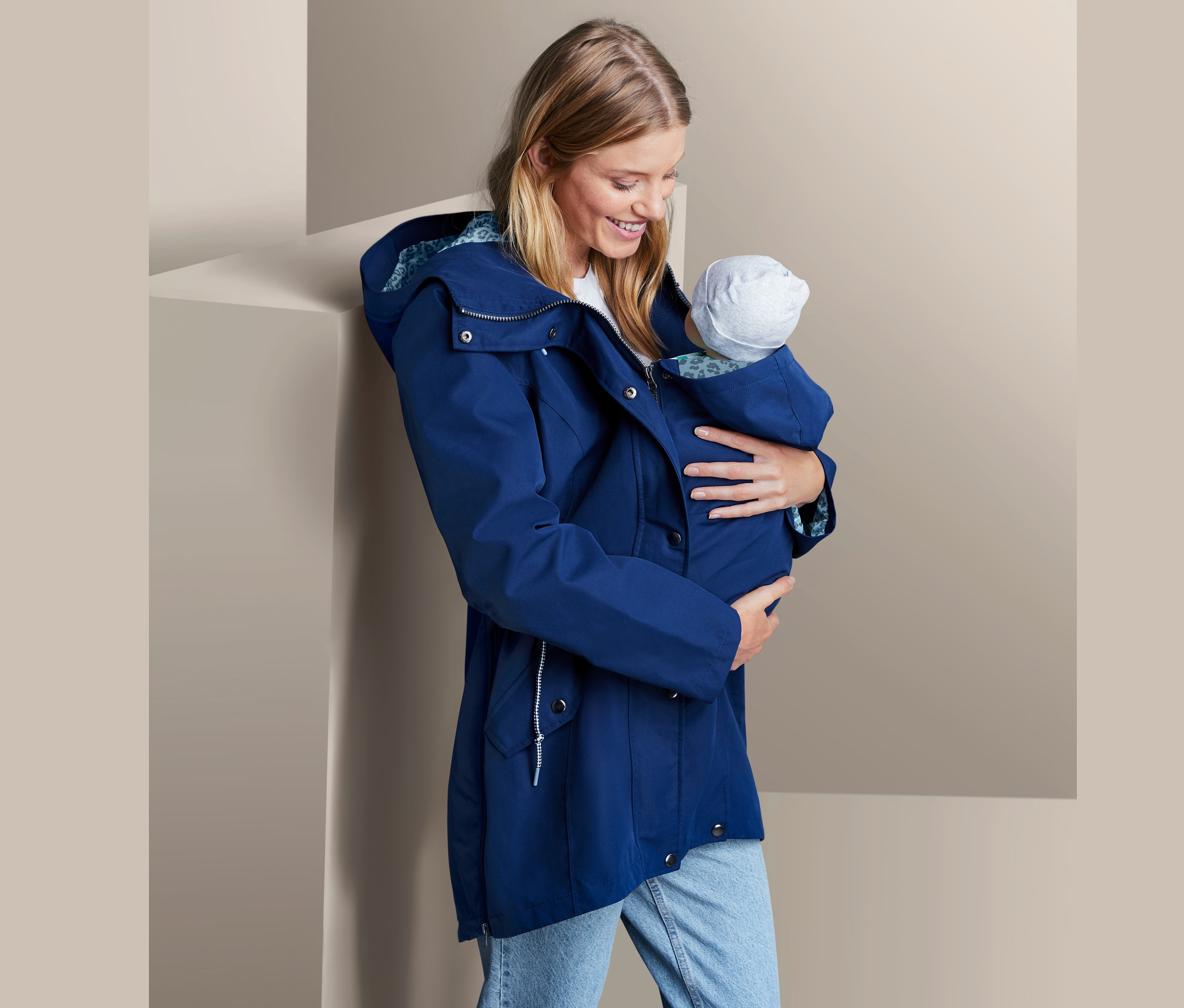 Žena drží dieťa v tehotenskej bunde do dažďa.