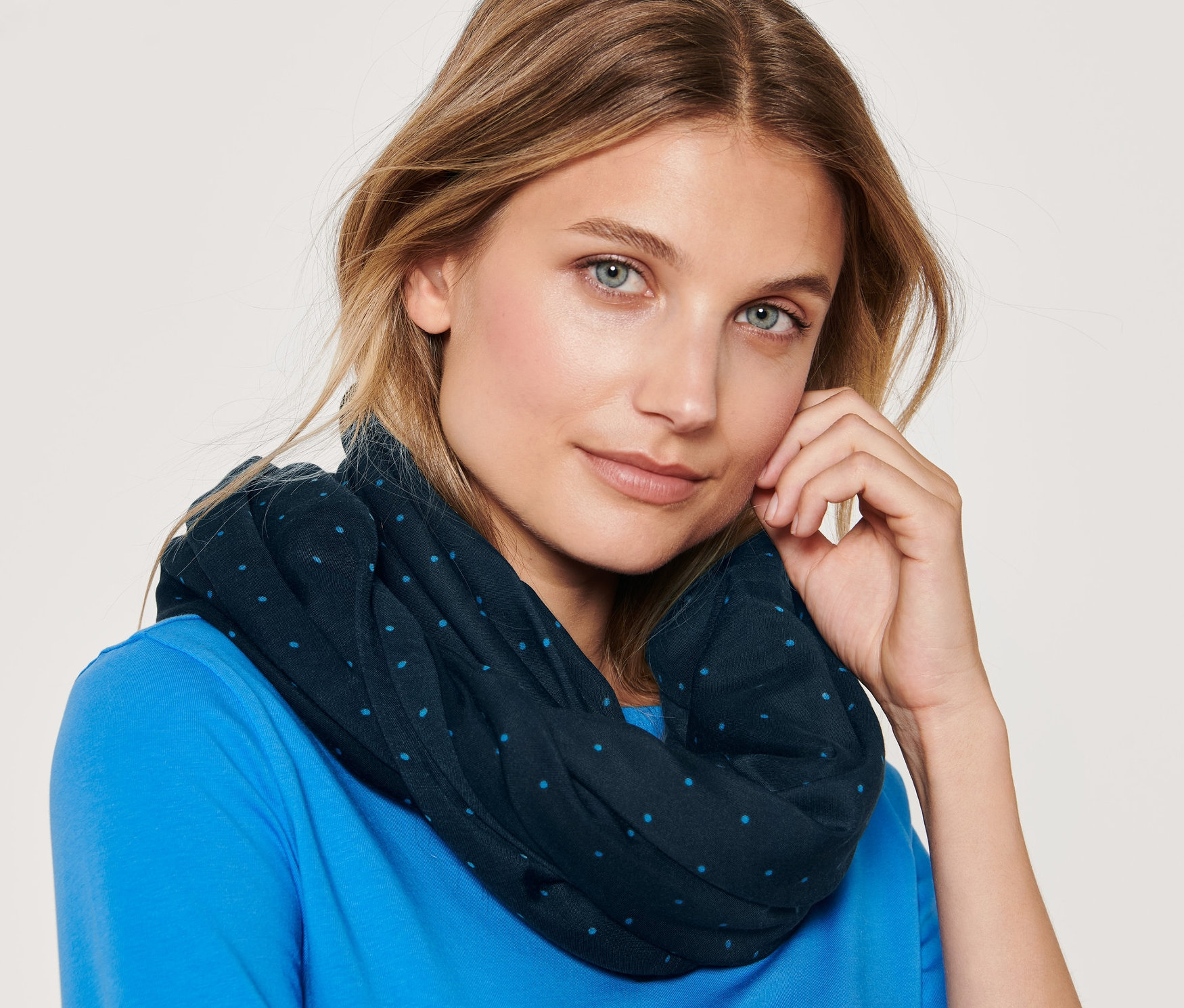 Portrét blondíny s modrými očami, ktorá má na sebe bodkovaný kruhový šál a modré tričko.
