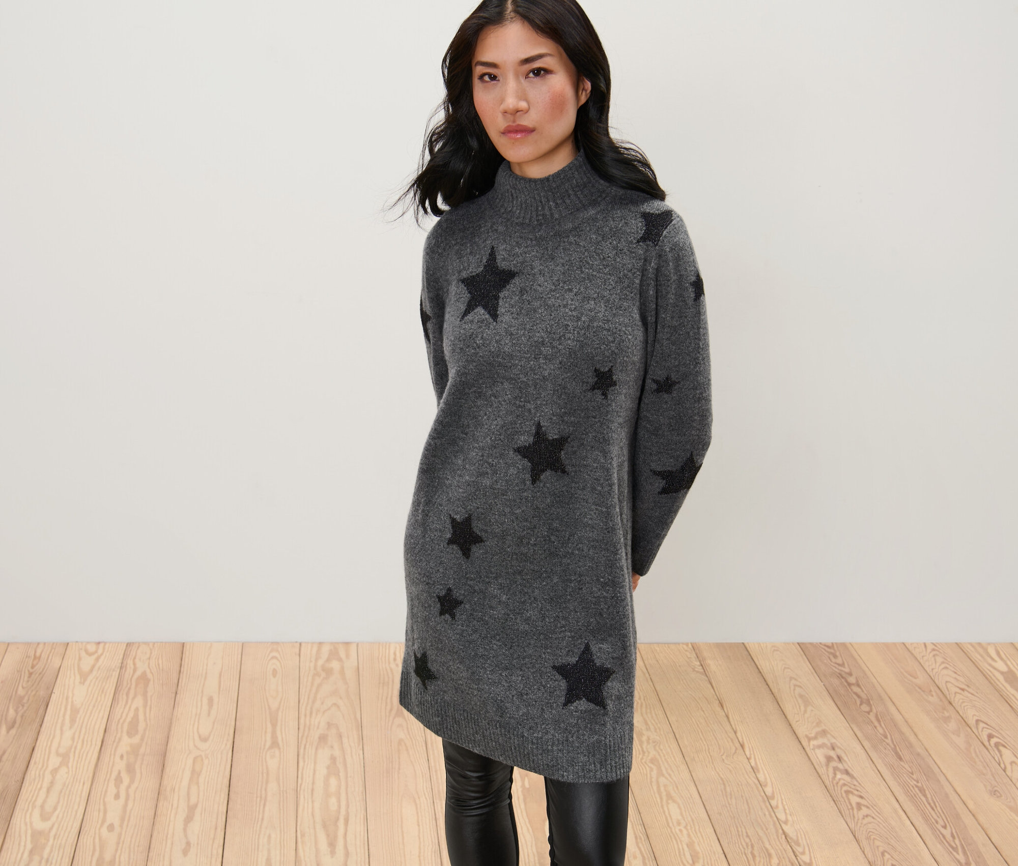Žena pózuje v pletených šatách s rolákovým golierom.